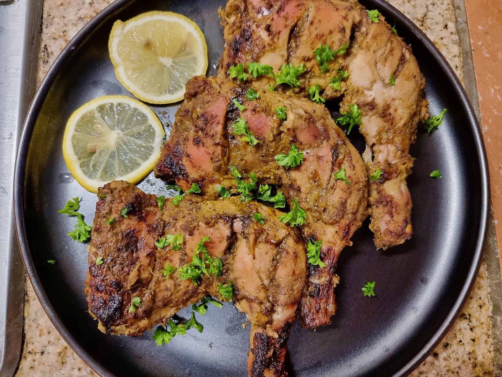 Arabic grilled chicken Al faham chicken that is garnished with parsley and serve with slices of lemon on a plate